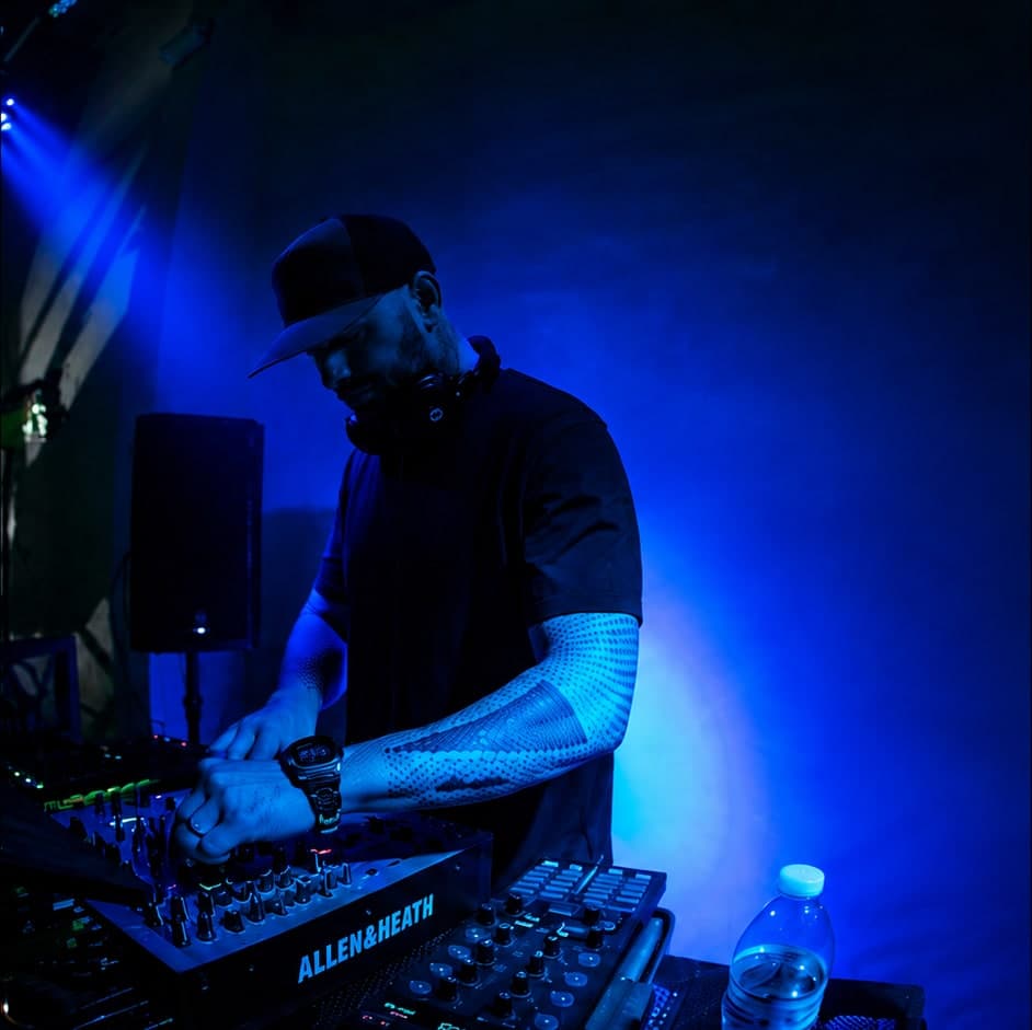 A DJ mixing on an Allen & Heath mixer under blue stage lighting