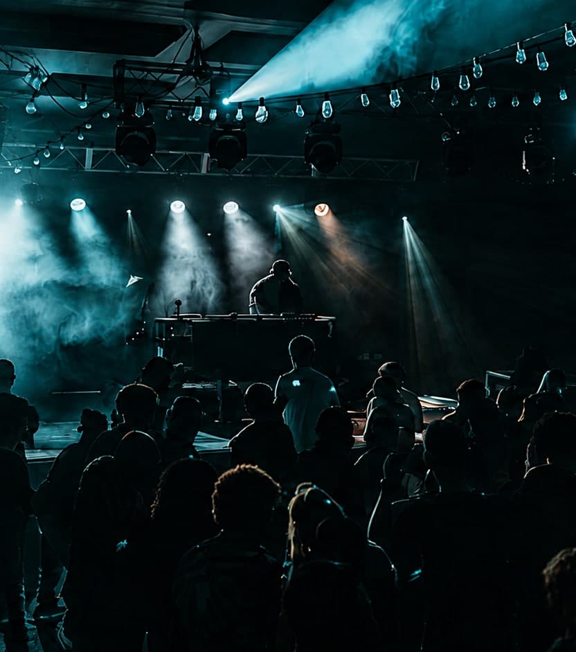 Wide view of a packed House Revival Project dance floor with a DJ performing under stage lights