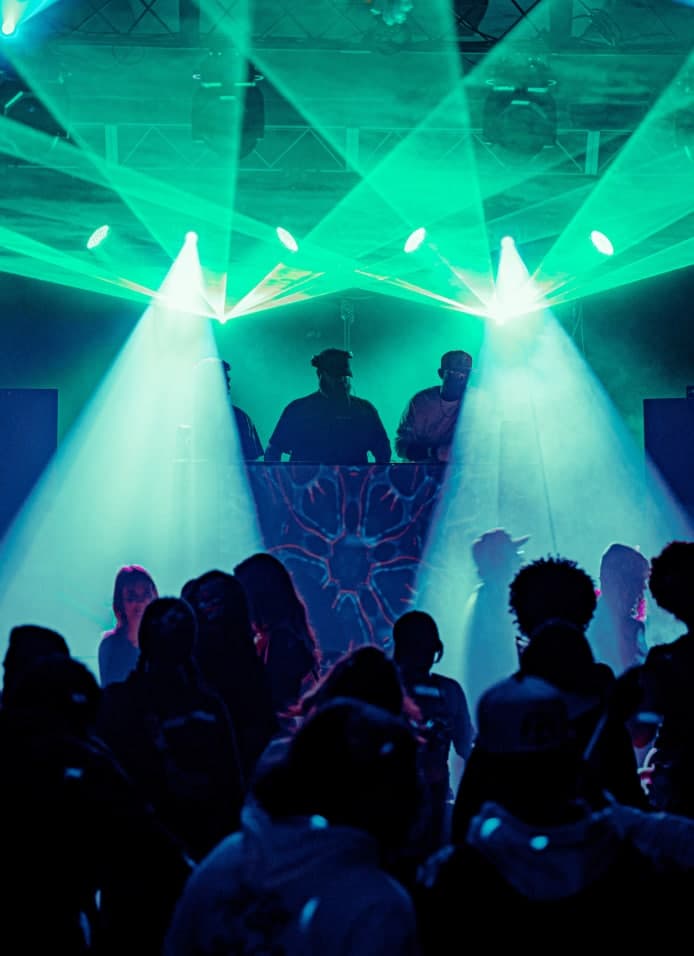 Three DJs performing under green laser lighting above a crowd at a House Revival Project event